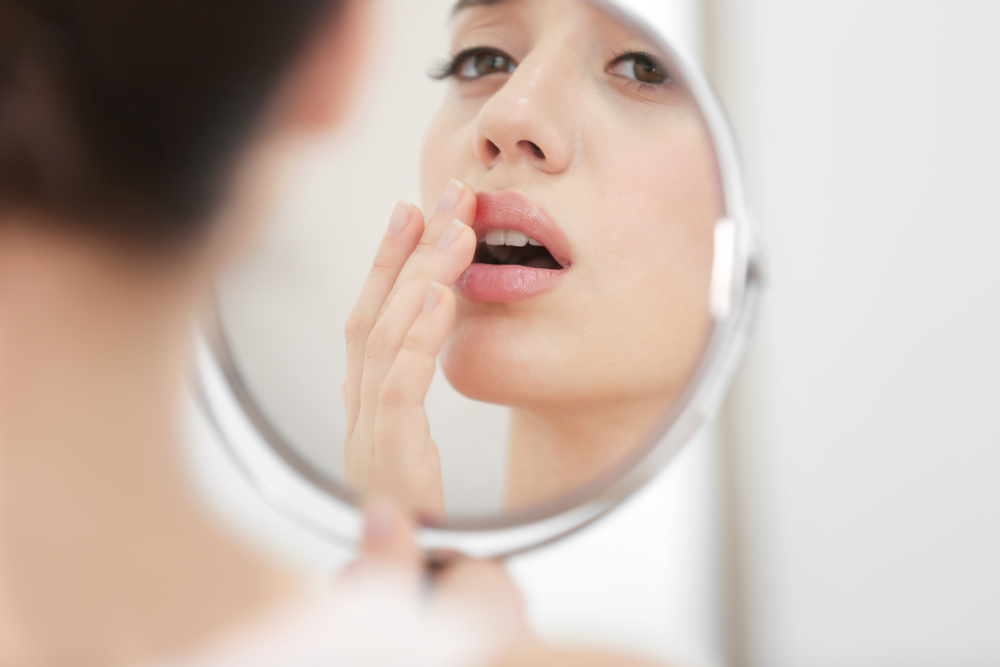 A woman with a cold sore caused by the herpes virus HSV2, examining her infected lip and wondering about treatment for cold sores