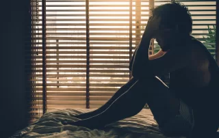 Depressed man sitting head in hands on the bed in a dark bedroom with low light environment