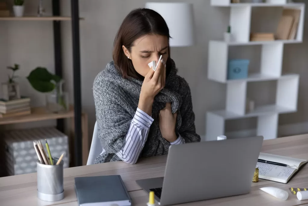 Sick girl wrapped in scarf holding tissue at face and consulting doctor online on video call