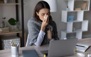 Sick girl wrapped in scarf holding tissue at face and consulting doctor online on video call