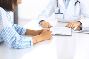 Doctor,And,Patient,Talking,And,Discussing,Health,Treatment,While,Sitting Young female doctor in white medical uniform with stethoscope using laptop for online consultation with a patient