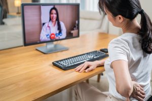 Sick girl wrapped in scarf holding tissue at face and consulting doctor online on video call